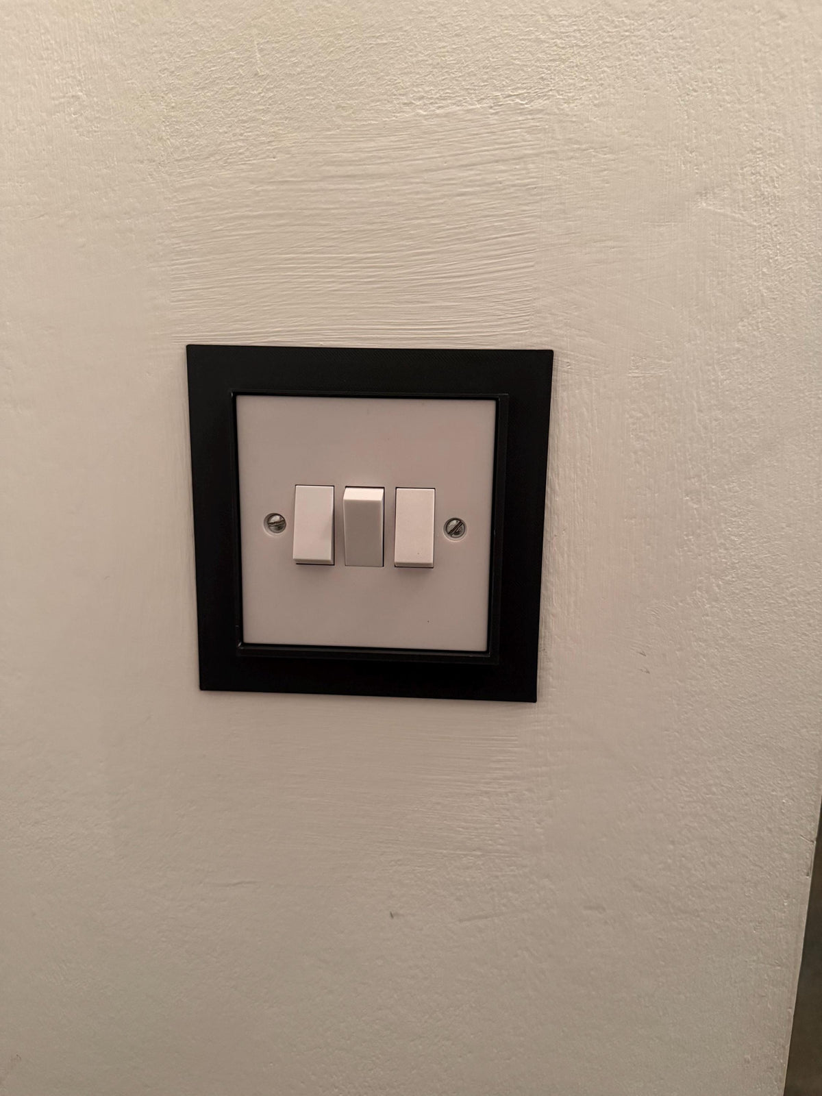 Black light switch frame cover fitted over a double light switch, straight-on view