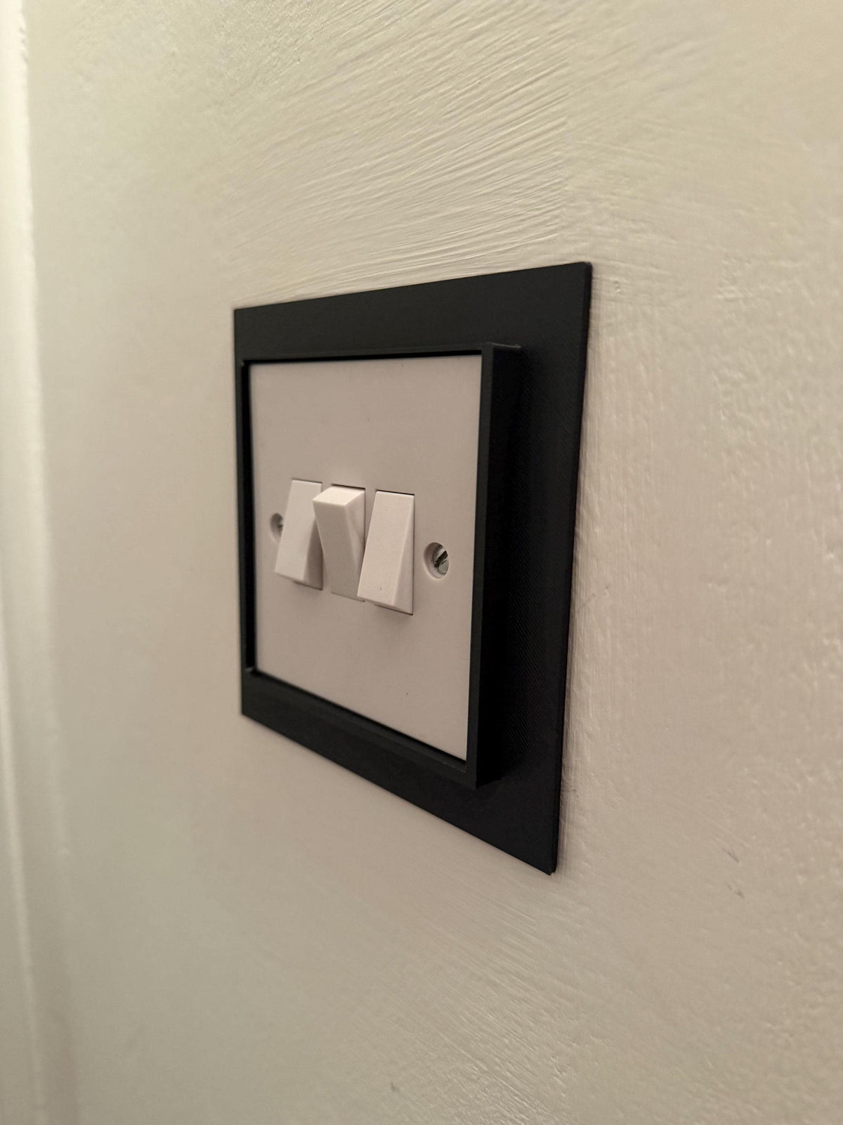 Black light switch frame cover fitted over a double light switch, angled view