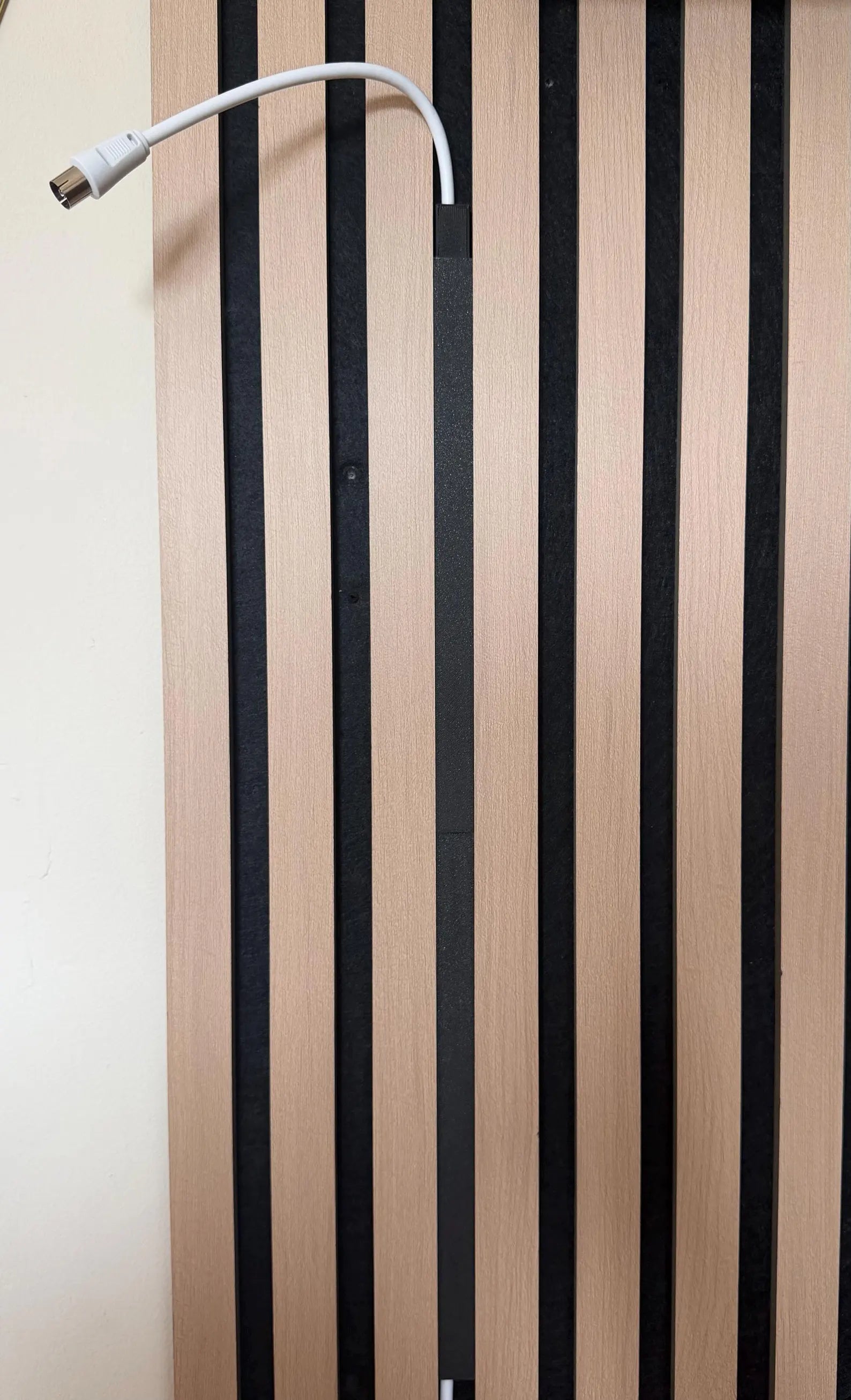 Black interlocking cable duct cover fitted into the gaps of a slat wall panel running vertically