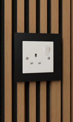 White single-gang socket surround fitted over a UK socket on an acoustic slat wall panel