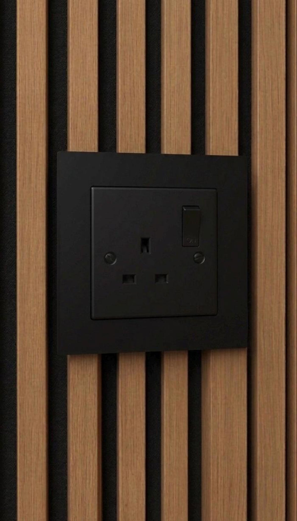 Black single-gang socket surround fitted over a UK socket on an acoustic slat wall panel