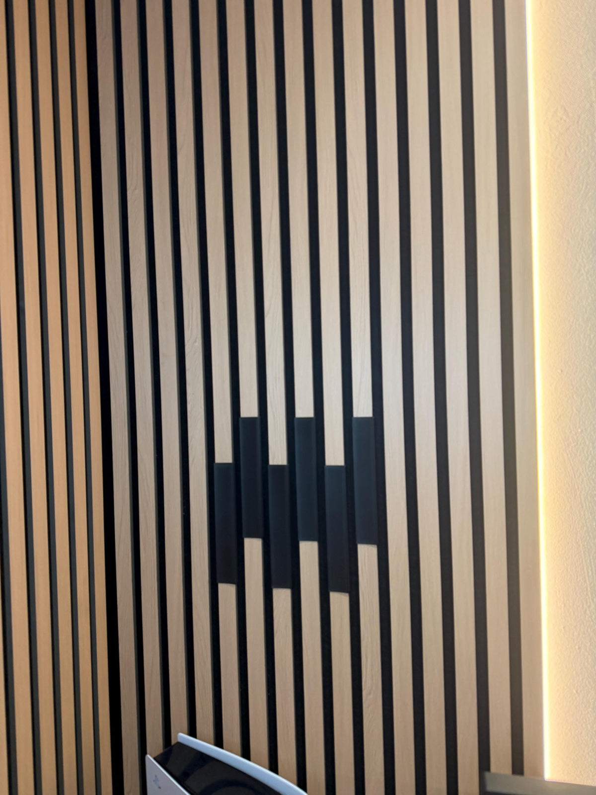 Black acoustic panel cable cover fitted into a slat wall gap, close-up