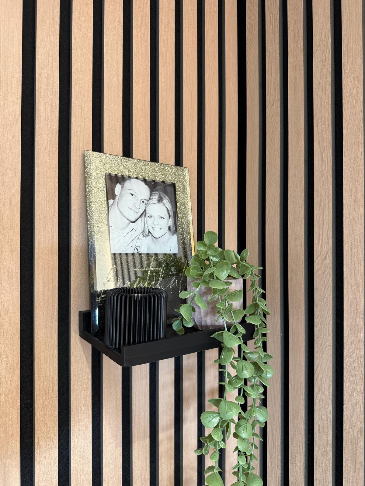Picture ledge shelf with framed photo and plant mounted on a slat wall, angled view