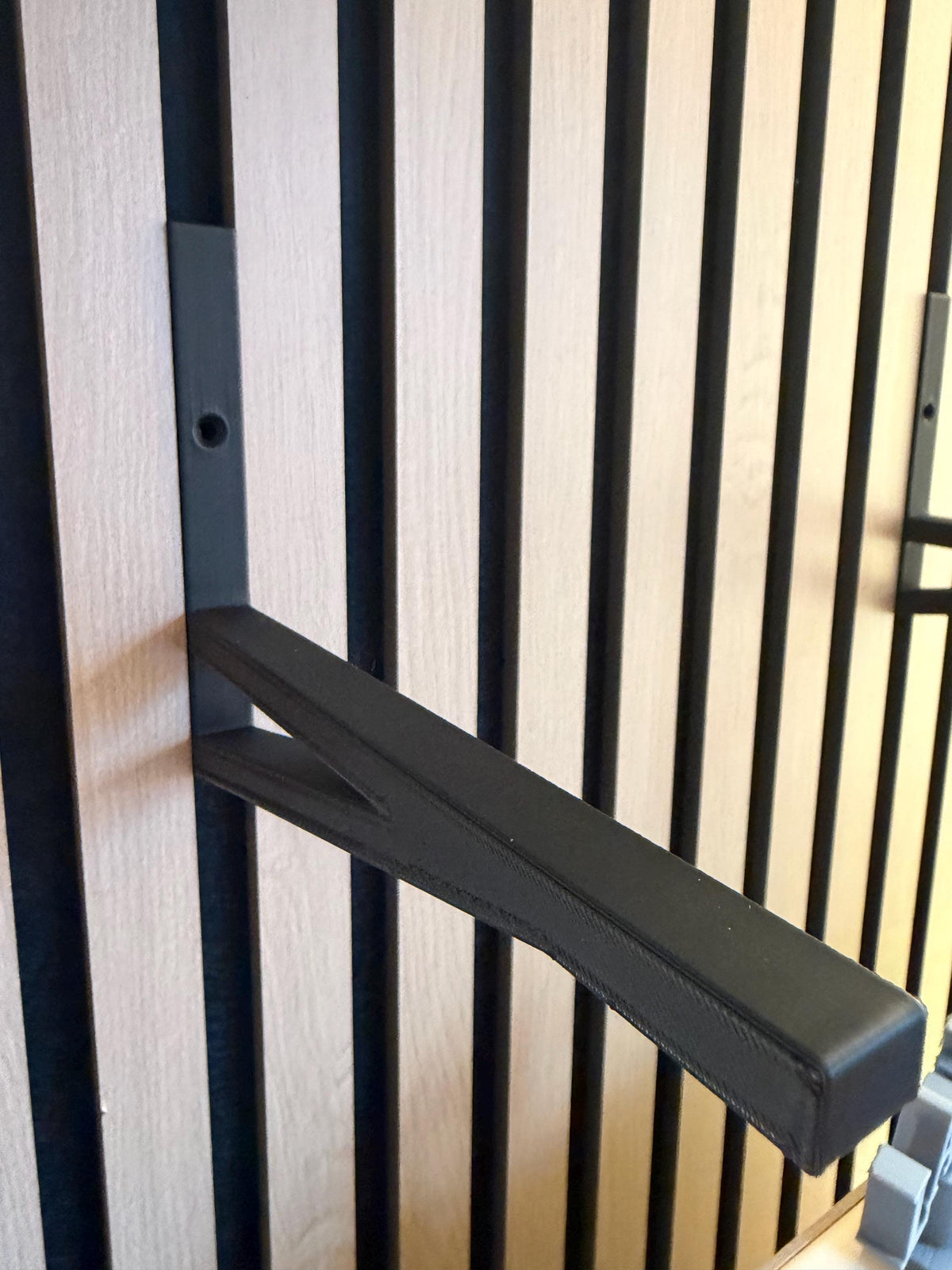 Black shelf bracket mounted on a slat wall panel, angled view