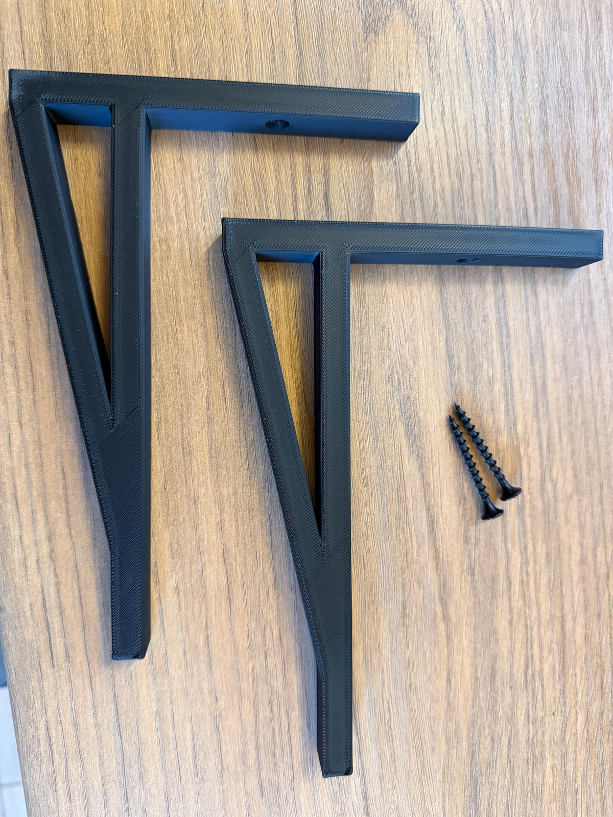 Pair of black shelf brackets and a fixing screw laid flat on a wood surface