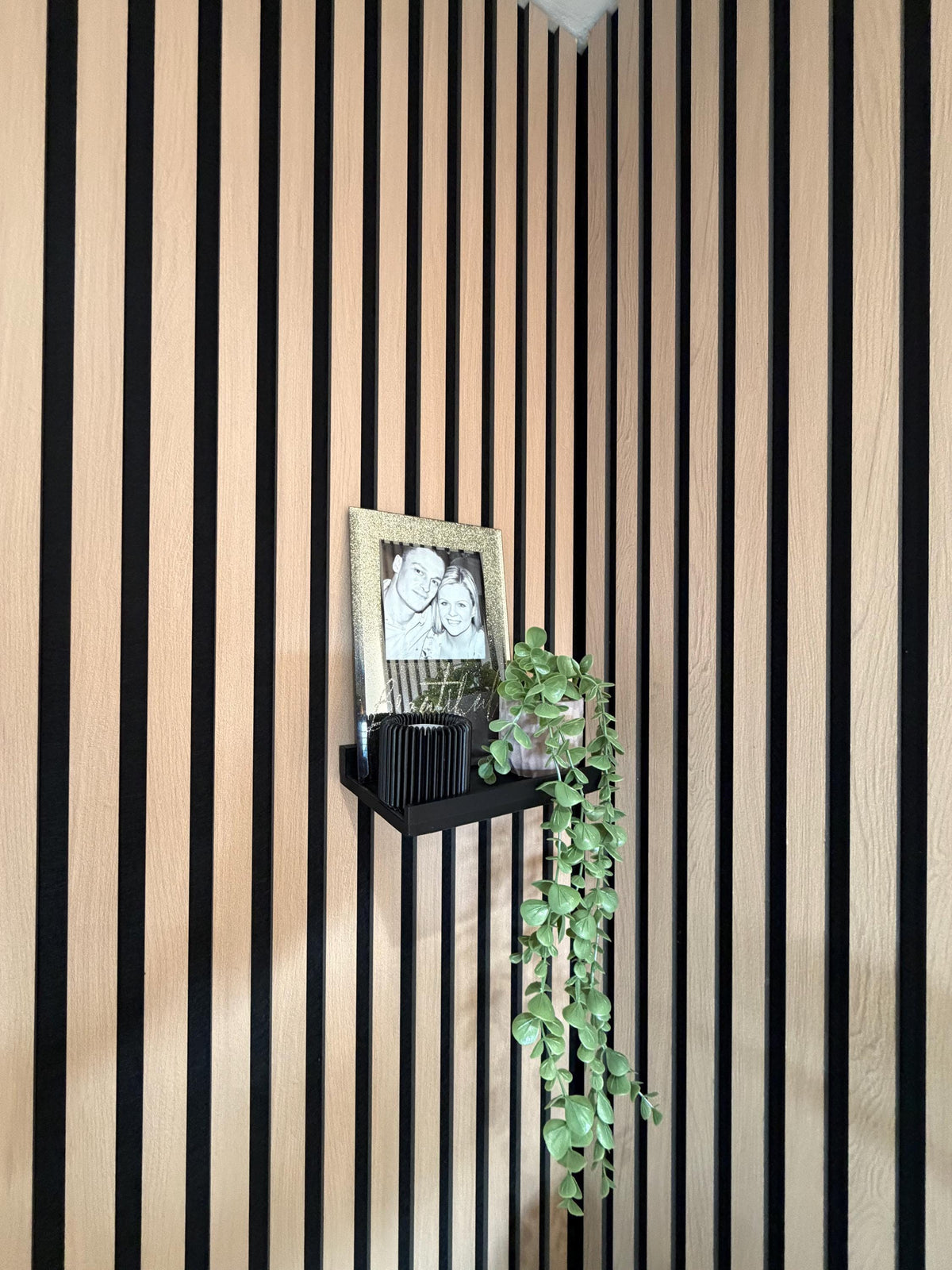 Picture ledge shelf with framed photo mounted on an acoustic slat wall panel, straight-on view