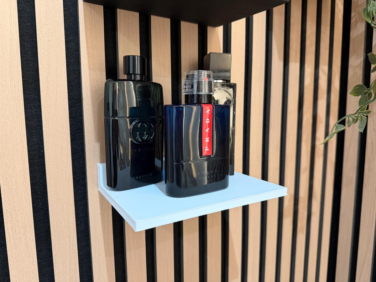 White perfume shelf on a slat wall displaying dark-coloured fragrance and grooming bottles