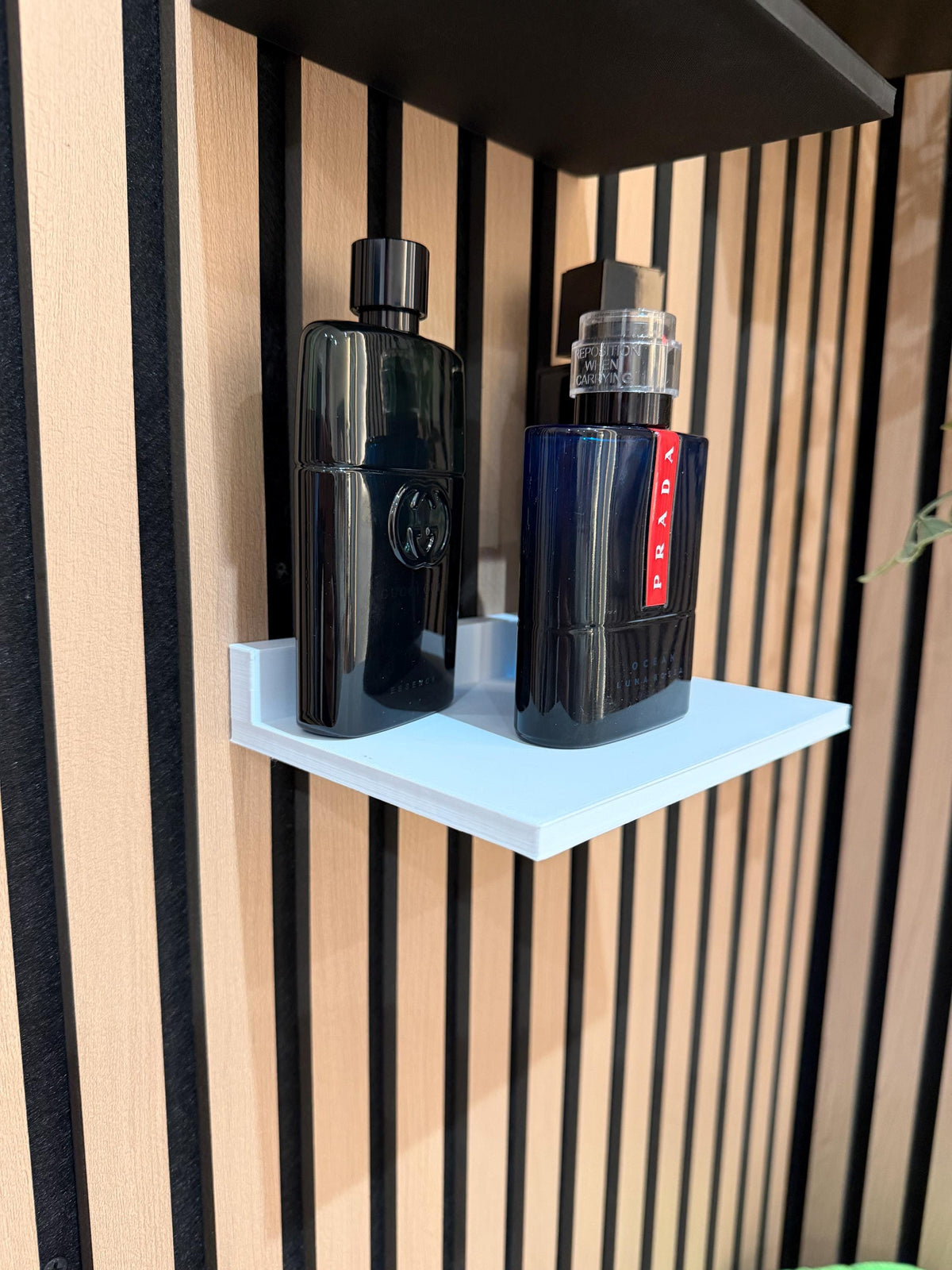 White perfume shelf on a slat wall displaying dark fragrance bottles, angled view
