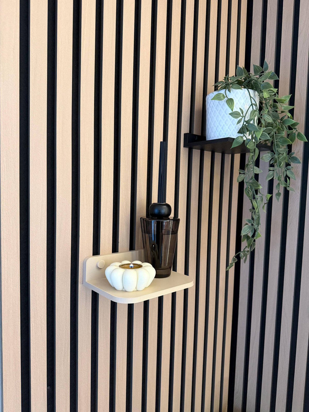 Beige floating shelf on a slat wall styled with a small plant, candle and pumpkin ornament