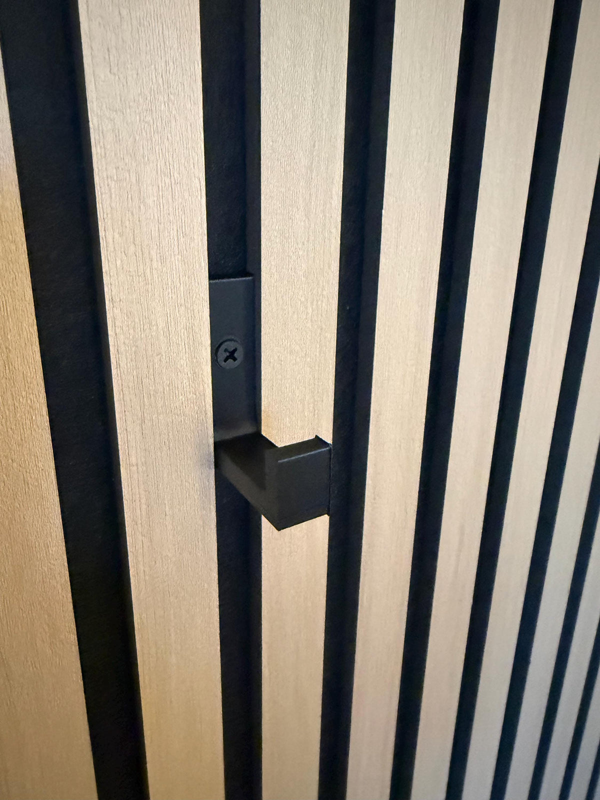 Matte black hook mounted on a slat wall panel, front view