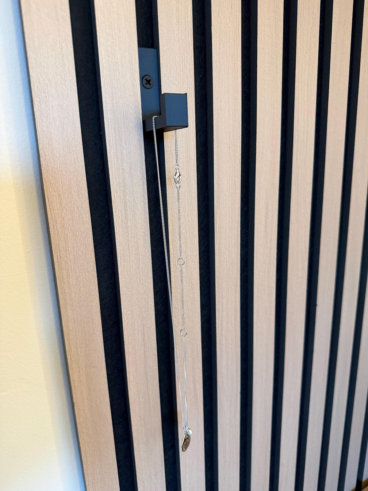 Matte black hook mounted on a slat wall panel with a set of keys hanging from it
