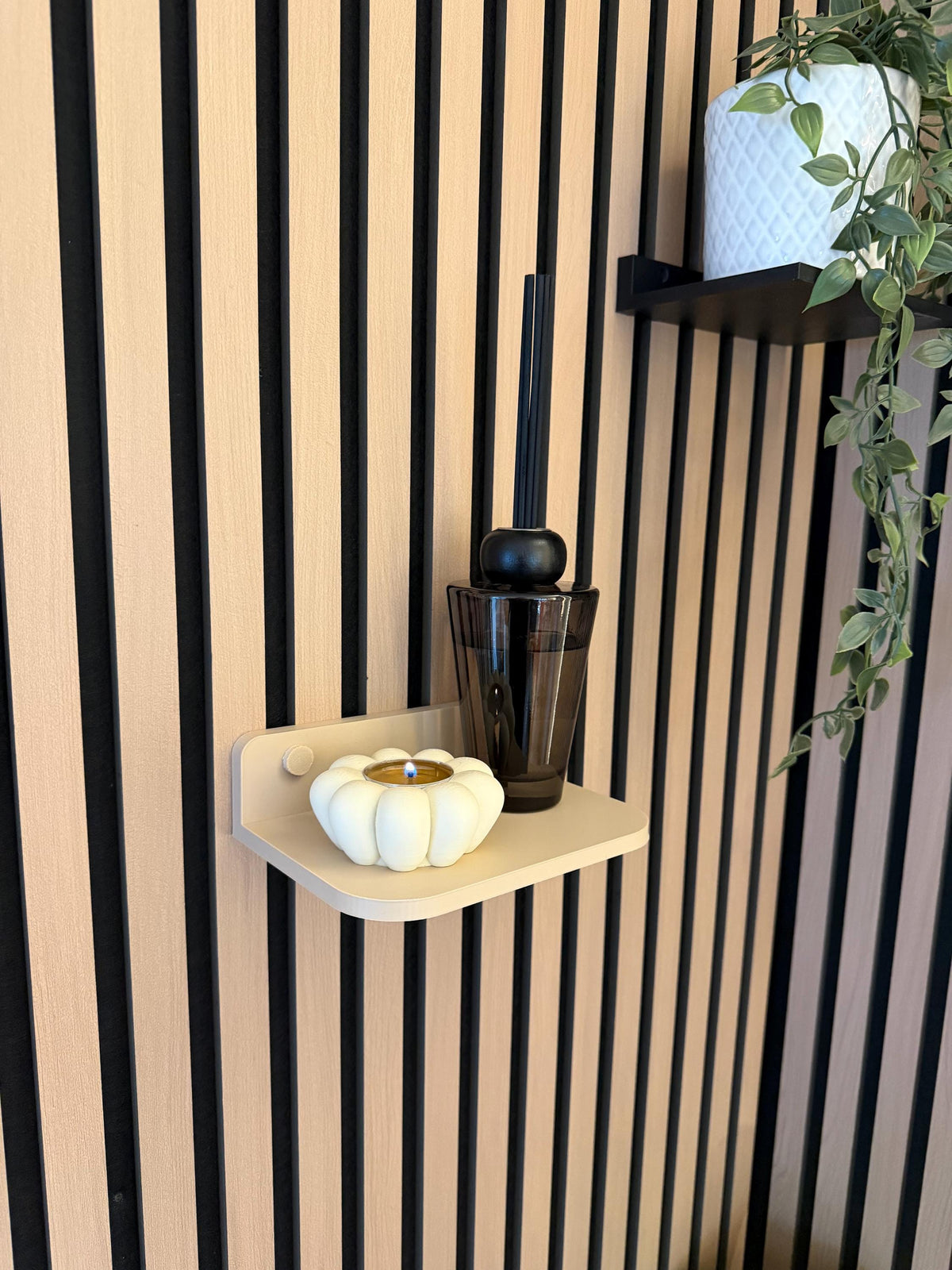 Beige floating shelf on a slat wall styled with a hanging plant and candle