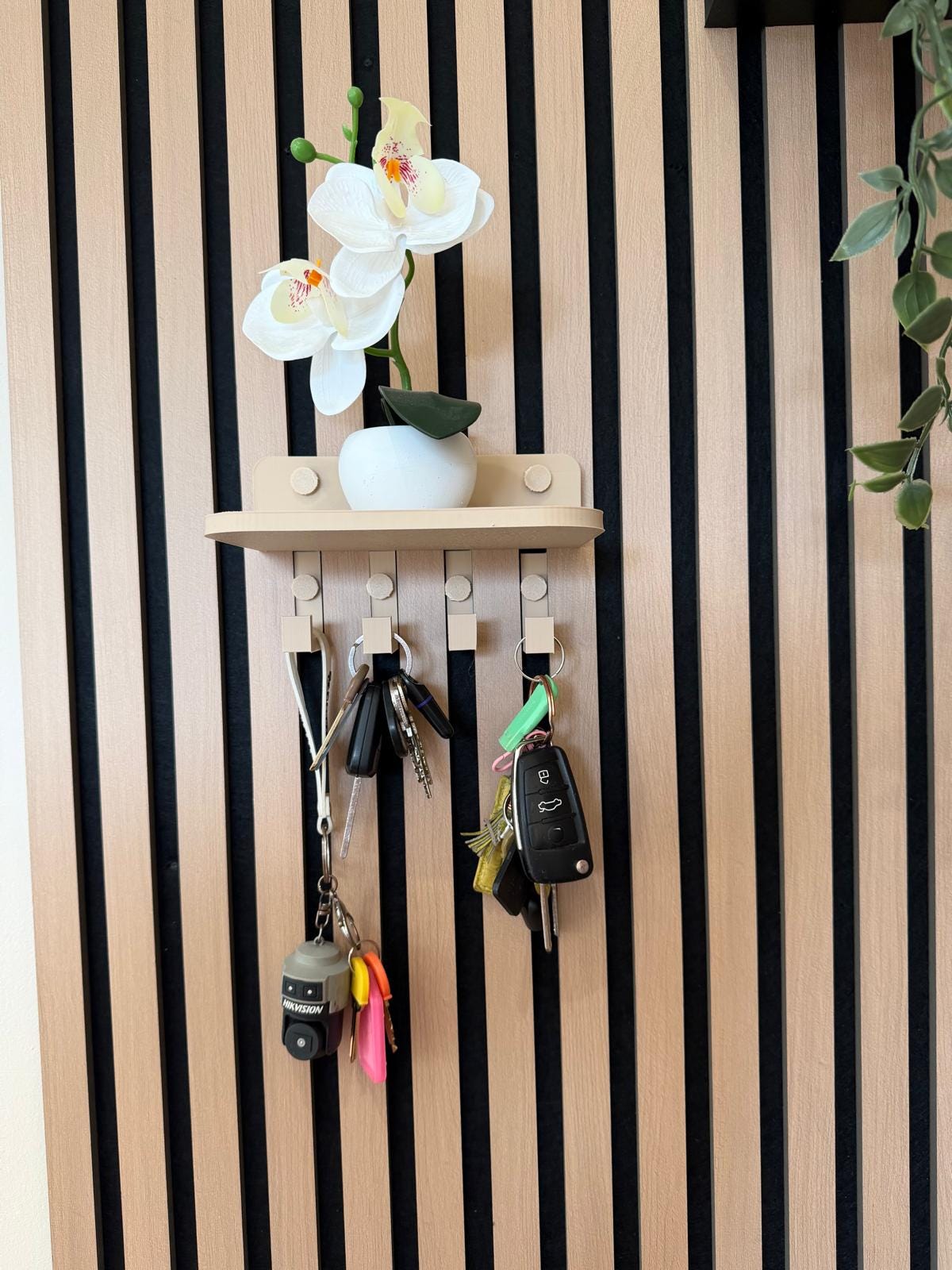 Key holder shelf on a slat wall styled with an orchid, vase and hanging keys