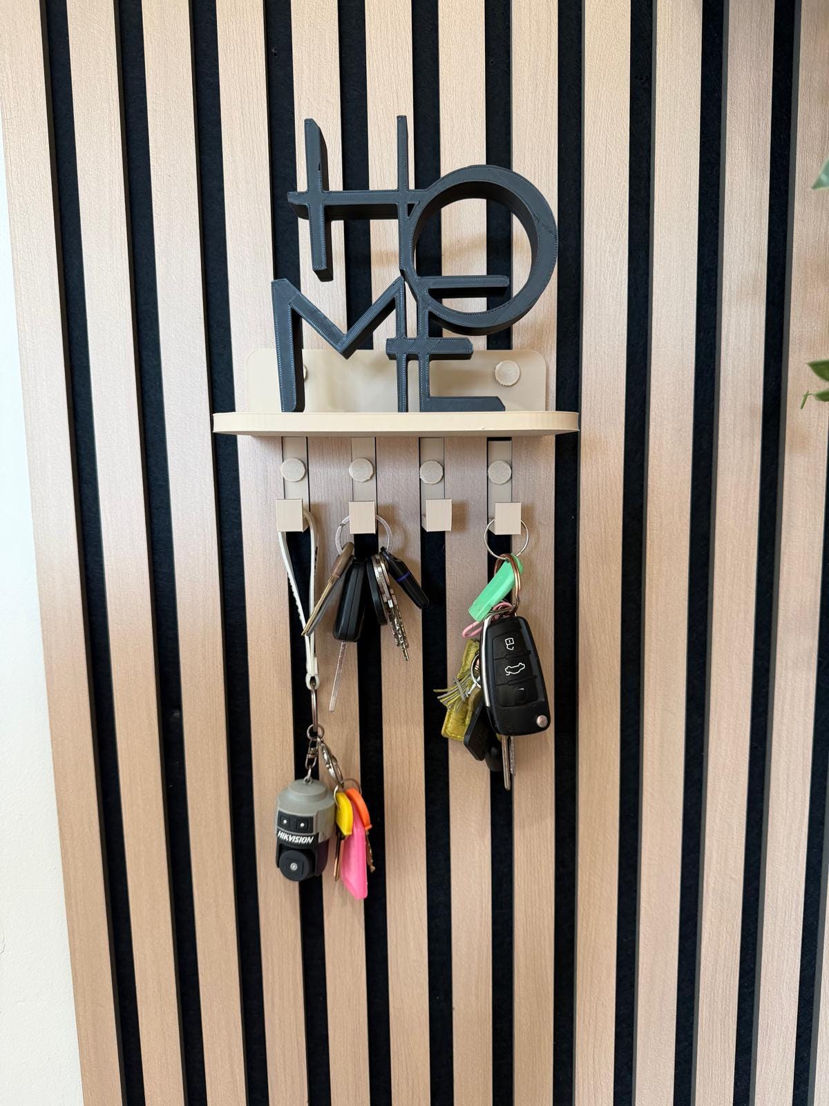 Key holder shelf on a slat wall styled with a plant, vase and hanging keys, close angle